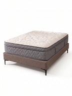 A mattress on a low upholstered bed frame with dark legs, photographed on a clean white studio background. The mattress has a quilted off-white top and a gray quilted side, while the bed base is taupe-brown.