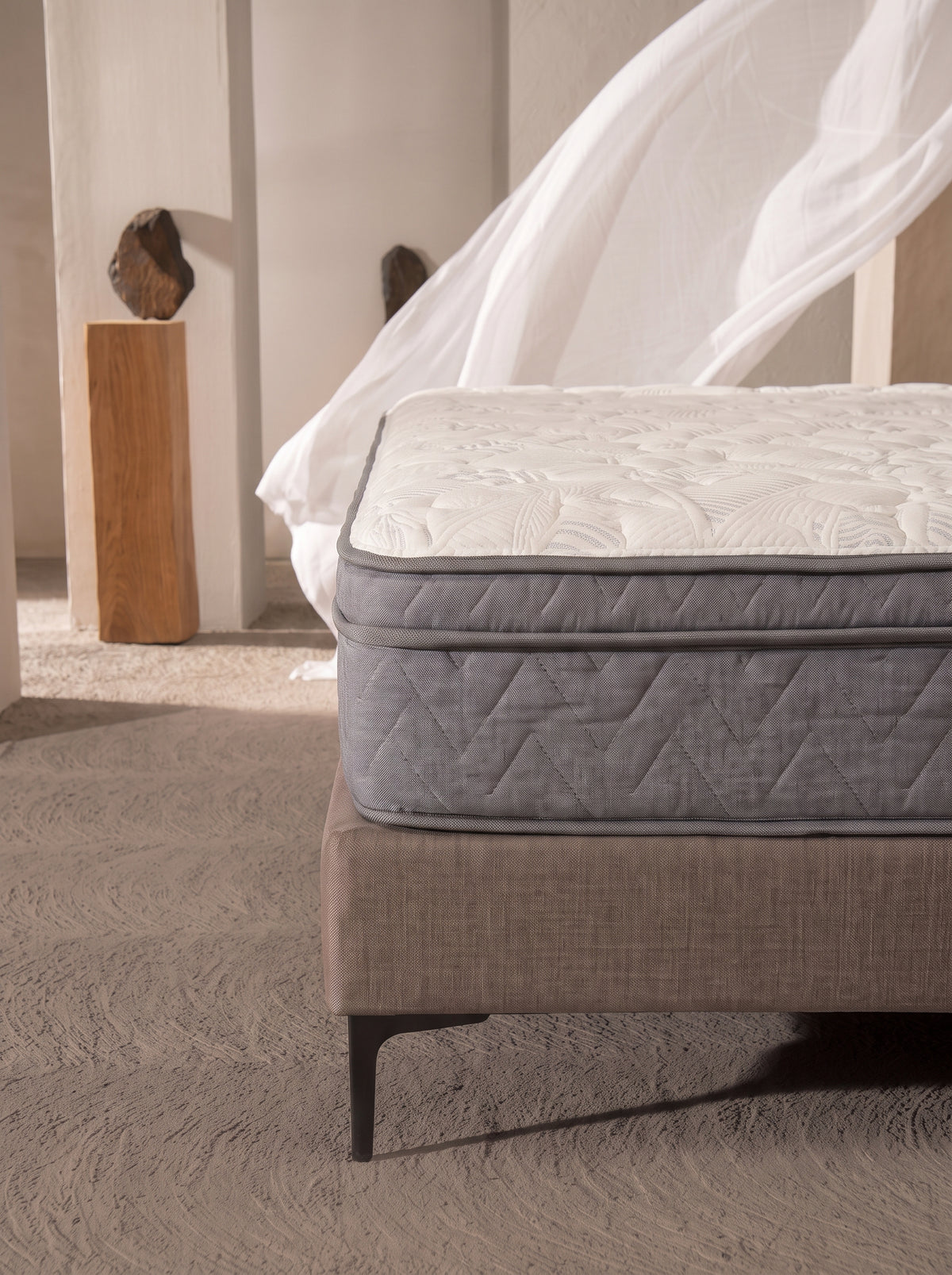 A quilted mattress on a upholstered bed frame in a softly lit bedroom setting with a white canopy and neutral decor.